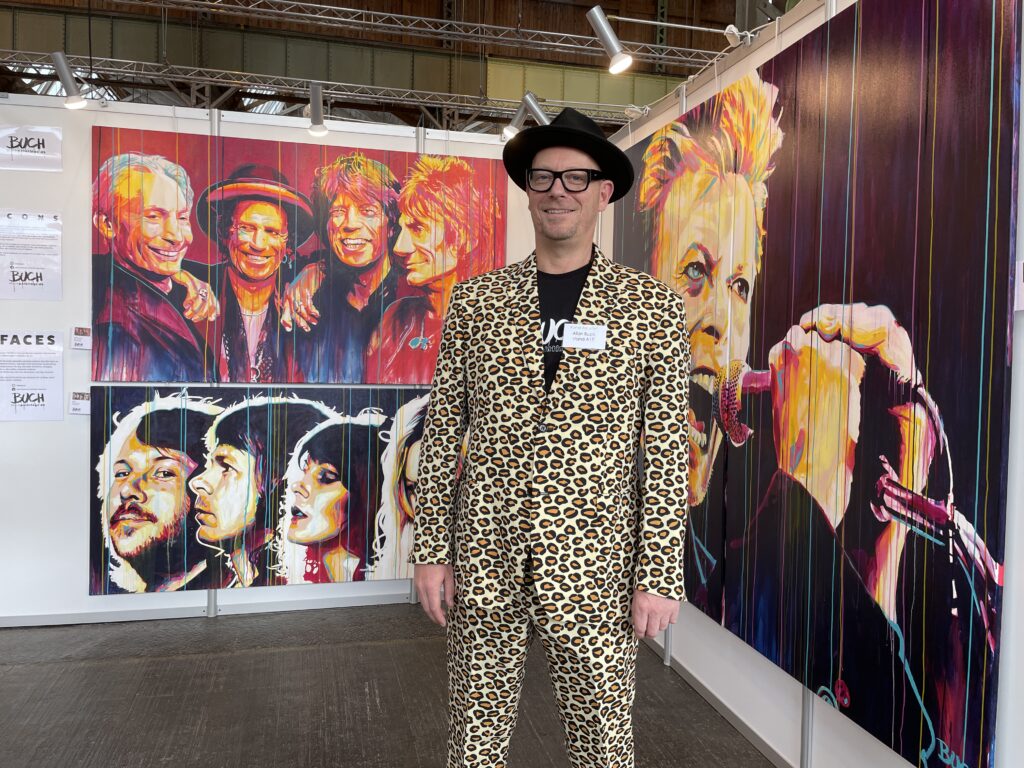 Allan Buch foran sine farverige malerier på en udstilling med malerier malerier med David Bowie, stones og ABBA i kraftige farver