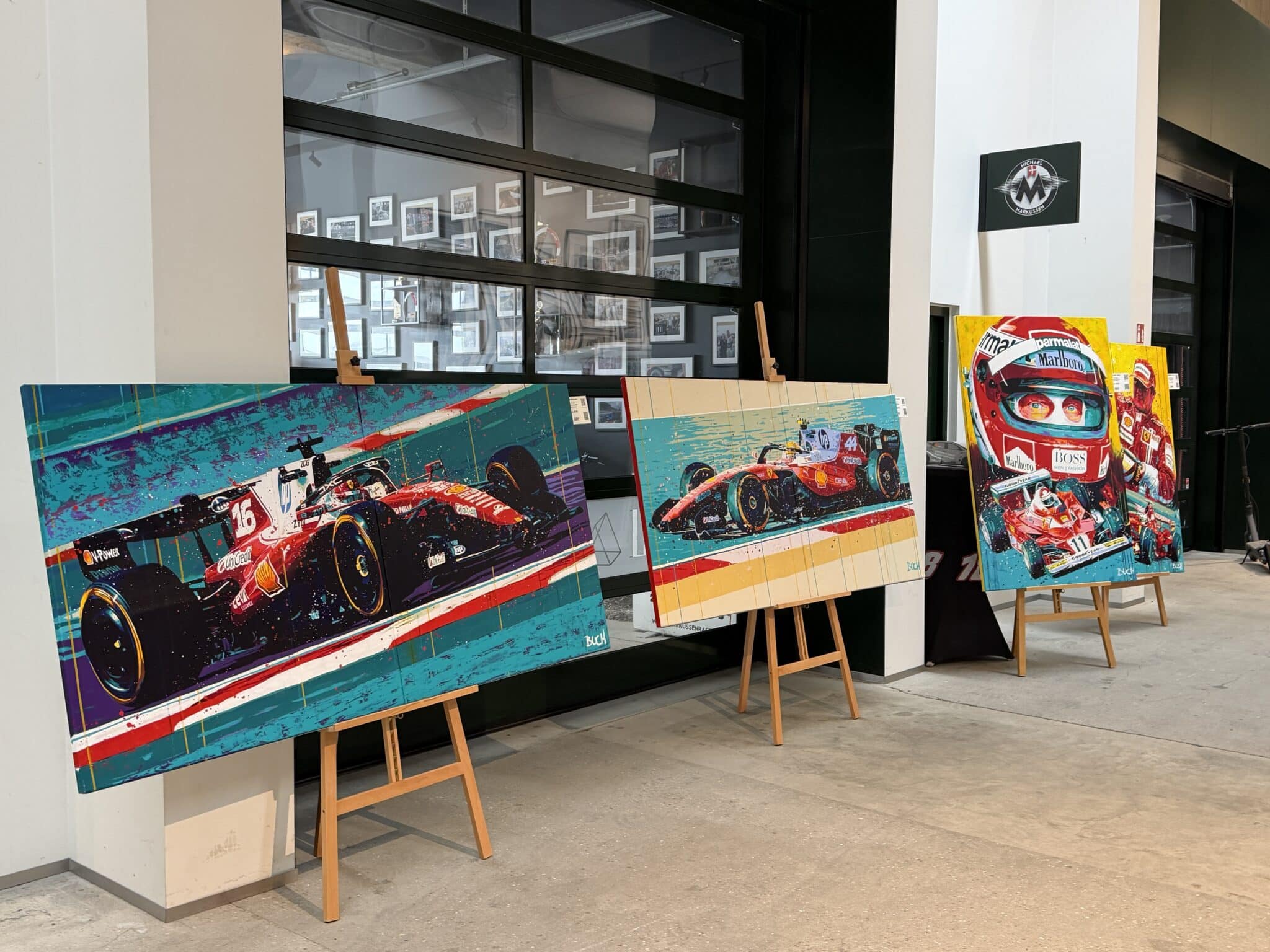 Colorful racing car paintings on wooden easels in a bright gallery space.